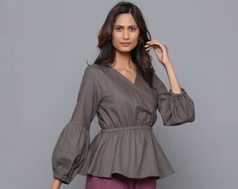 May include: A gray wrap top with a V-neckline and long sleeves. The sleeves have a gathered, puffed look. The top has a fitted bodice and a flowing, slightly flared hemline. The top is cinched at the waist with a thin elastic band.