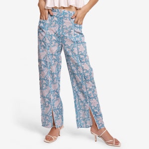May include: Blue wide-leg pants with a white floral print and side slits. The pants have a white trim along the seams.