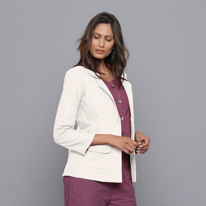 May include: A white blazer with a single button fastening and a pocket on the left side. The blazer has long sleeves and a collar.
