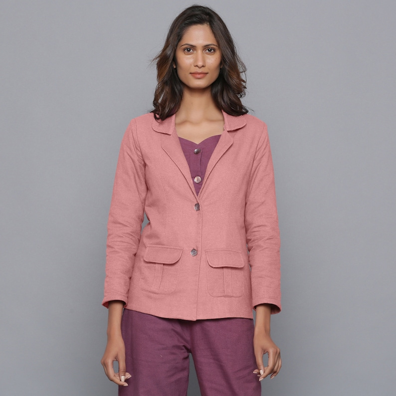 May include: A dusty rose blazer with two front pockets and a two-button closure. The blazer is paired with a purple top and pants. The outfit is a casual, yet stylish ensemble.
