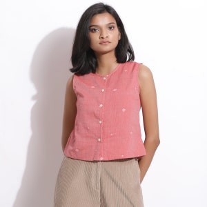 Puede incluir: Una blusa rosa sin mangas con botones y un estampado floral blanco. La blusa est&aacute; hecha de una tela ligera y tiene un corte holgado.