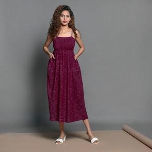 May include: A burgundy maxi dress with thin straps and a gathered waist. The dress has a subtle textured pattern and is made of a soft, flowing fabric.