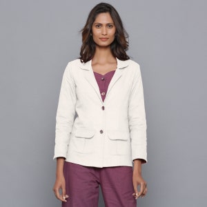 May include: A cream-colored blazer with two front pockets and matching buttons. The blazer is worn over a plum-colored top and pants. The outfit is a neutral color palette, suitable for a variety of occasions.