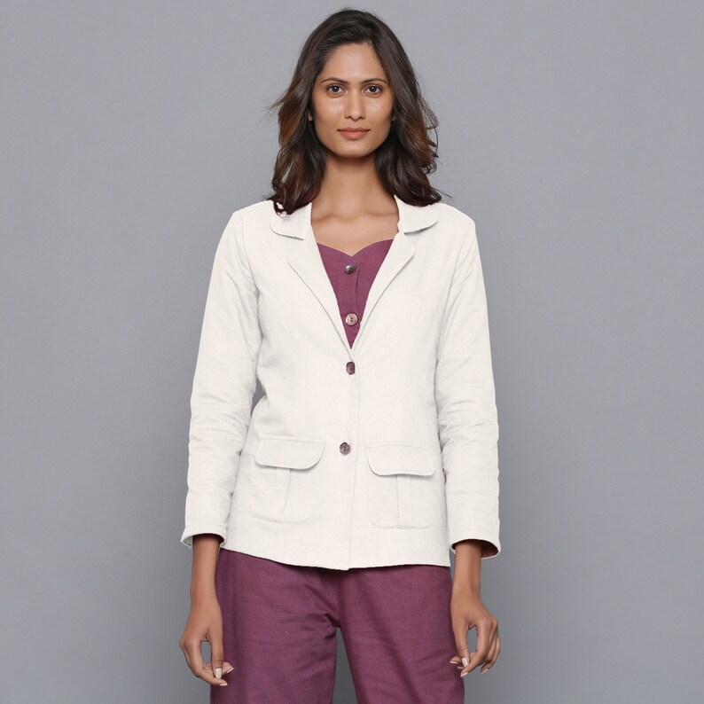May include: A cream-colored blazer with two front pockets and matching buttons. The blazer is worn over a plum-colored top and pants. The outfit is a neutral color palette, suitable for a variety of occasions.