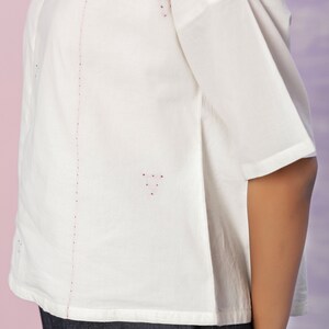 May include: White cotton shirt with short sleeves and a red dotted design. The shirt has a straight hem and a slightly loose fit.