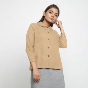 May include: A beige long-sleeved collared shirt with a button-up front and a peter pan collar.