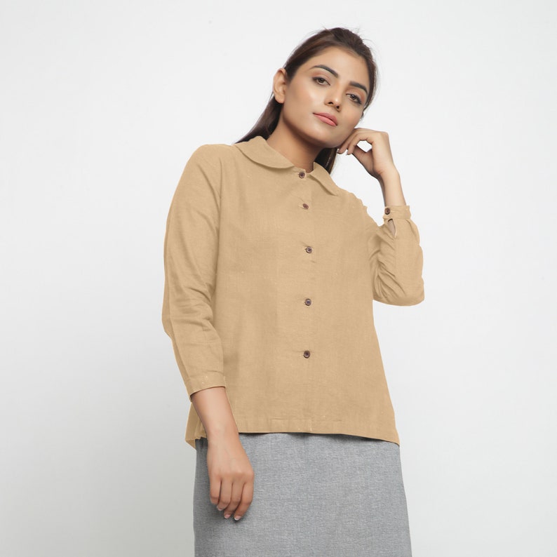 May include: A beige long-sleeved collared shirt with a button-up front and a peter pan collar.