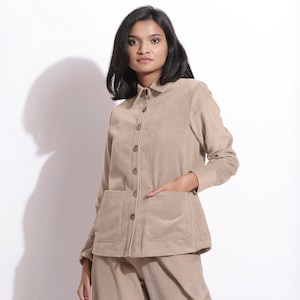 Pode incluir: Uma camisa de veludo cotelê bege com fecho de botões e dois bolsos de remendo. A camisa tem mangas compridas e gola.