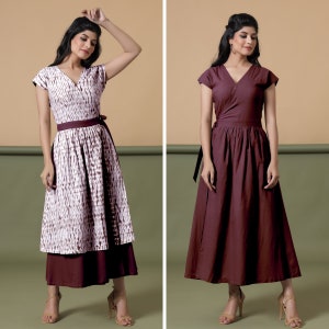 Könnte beinhalten: Zwei Frauen tragen lange Wickelkleider. Das Kleid links ist weiß mit einem braunen Batik-Muster und einem weinroten Unterrock. Das Kleid rechts ist einfarbig weinrot.