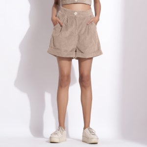 May include: Beige corduroy shorts with a button closure and side pockets. The shorts have a relaxed fit and a cuffed hem.