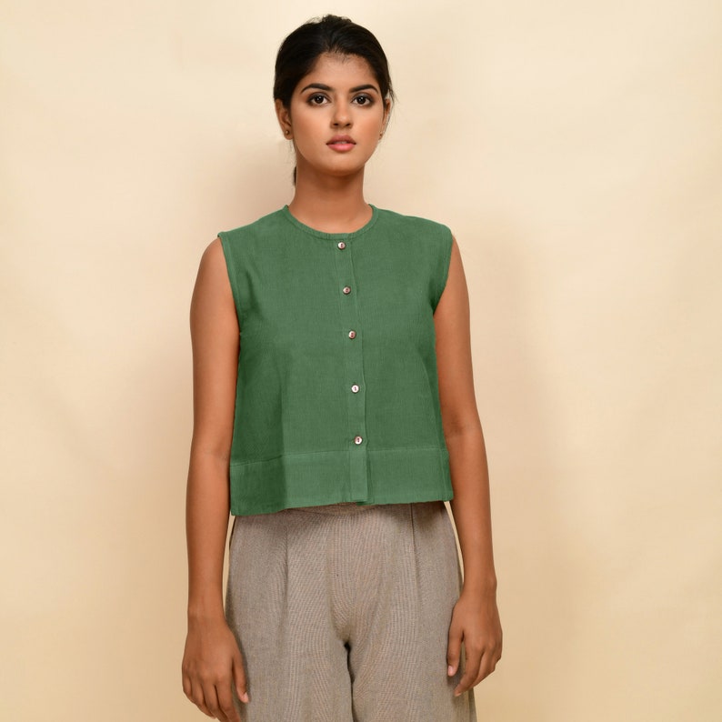 Puede incluir: Una blusa verde sin mangas con botones y cuello redondo. La blusa es corta y tiene un dobladillo recto.