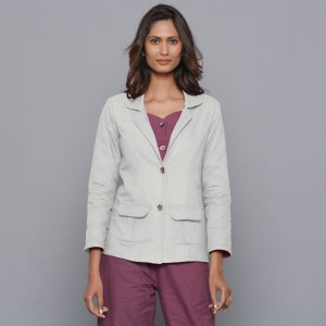 May include: A light gray blazer with two front pockets and matching buttons. The blazer is worn over a plum-colored top and paired with plum-colored pants. The outfit is set against a gray background.