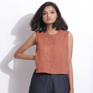 Puede incluir: Una blusa de lino sin mangas de color &oacute;xido con cierre de botones en la parte delantera. La blusa tiene un corte holgado y una longitud recortada.