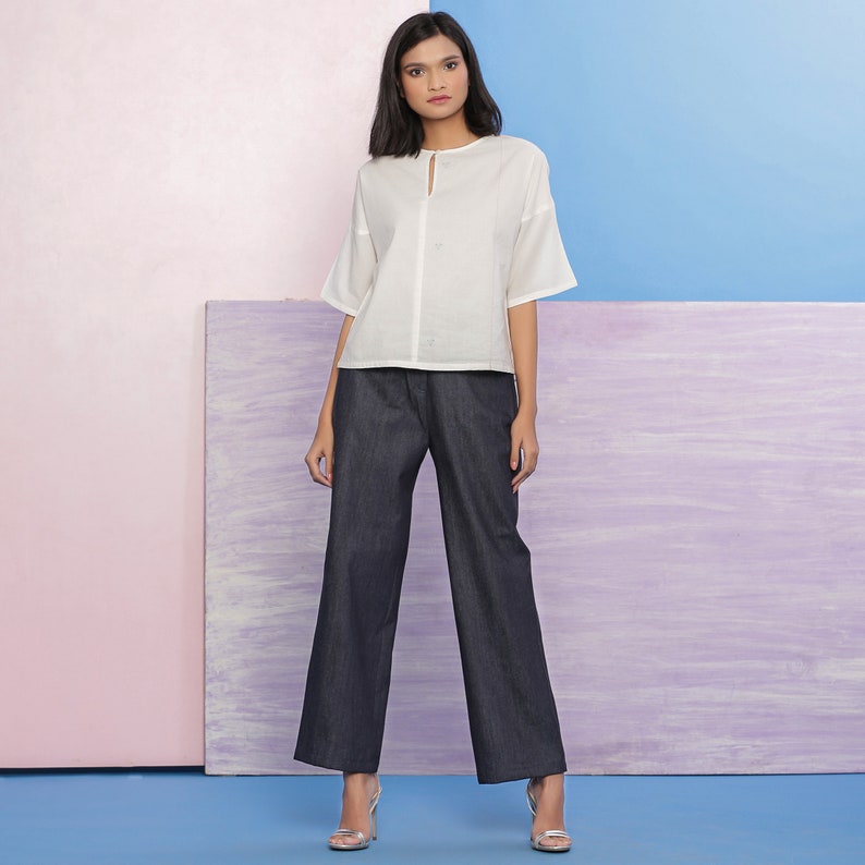 May include: A white button-down top with a keyhole neckline and short sleeves paired with dark blue wide-leg pants.