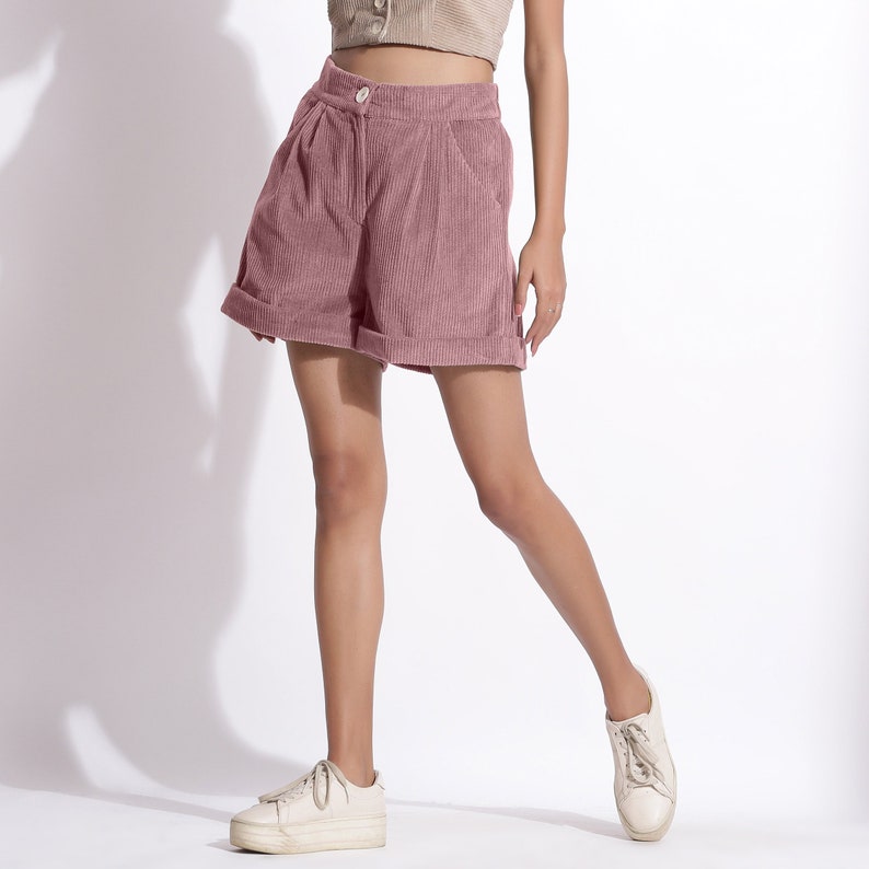 May include: A pair of pink corduroy shorts with a high waist and a button closure. The shorts have a relaxed fit and are cuffed at the hem.