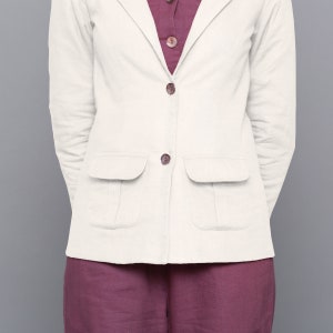 May include: A white linen blazer with two patch pockets and button fastenings. The blazer is worn over a burgundy top.