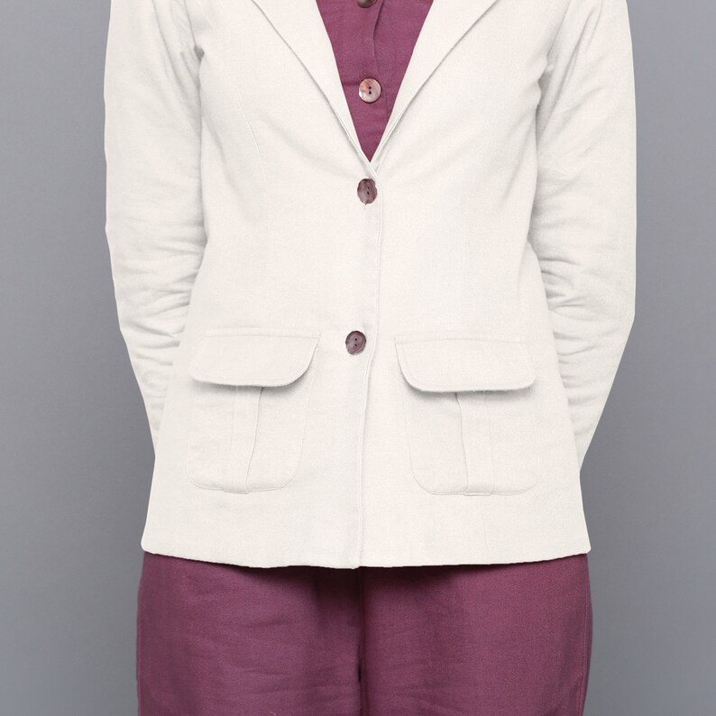 May include: A white linen blazer with two patch pockets and button fastenings. The blazer is worn over a burgundy top.