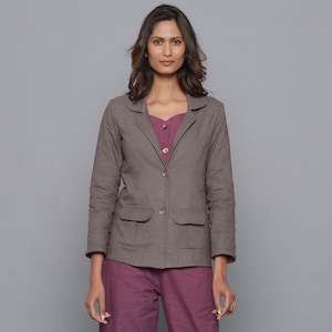 May include: A brown blazer with two front pockets and two buttons. The blazer is worn over a purple top and paired with matching purple pants. The outfit is set against a gray background.