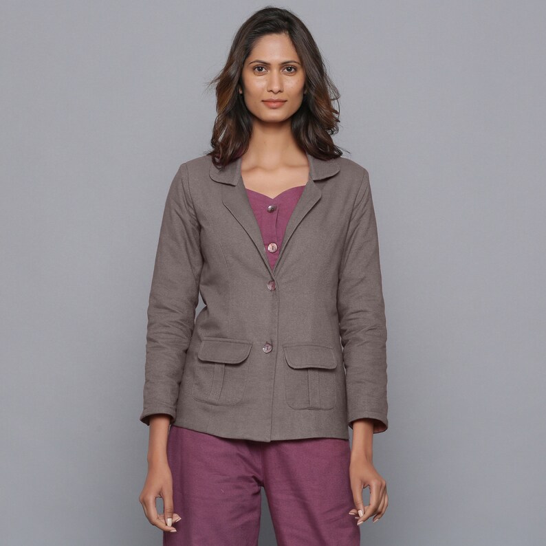 May include: A brown blazer with two front pockets and two buttons. The blazer is worn over a purple top and paired with matching purple pants. The outfit is set against a gray background.