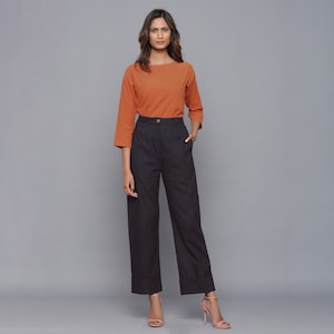 May include: A woman is wearing a rust-colored, three-quarter sleeve top with a black pair of wide-leg pants. The pants have a high waist and a button closure.