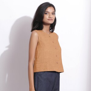 Puede incluir: Una blusa de lino marr&oacute;n sin mangas con cierre de botones en la parte delantera. La blusa tiene un escote redondo y una longitud recortada.