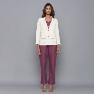 May include: A white linen blazer with a single button closure and two patch pockets. The blazer is worn over a burgundy top and trousers.
