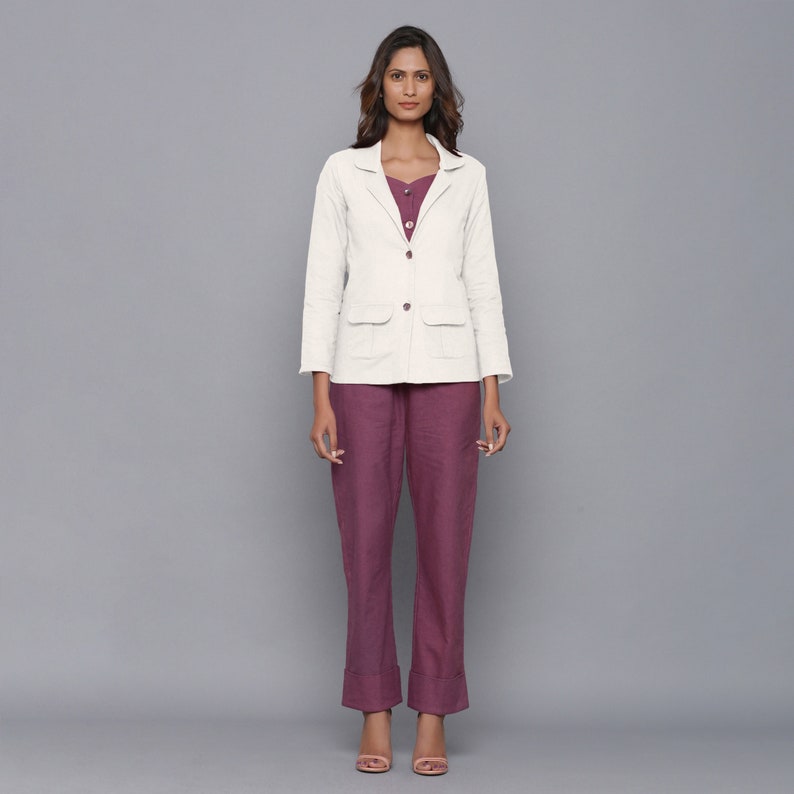 May include: A white linen blazer with a single button closure and two patch pockets. The blazer is worn over a burgundy top and trousers.