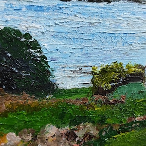 May include: A painting of a landscape with a lake in the background. The lake is a light blue color and the water is textured. There are green trees on either side of the lake. The foreground is a green grassy area with brown rocks.
