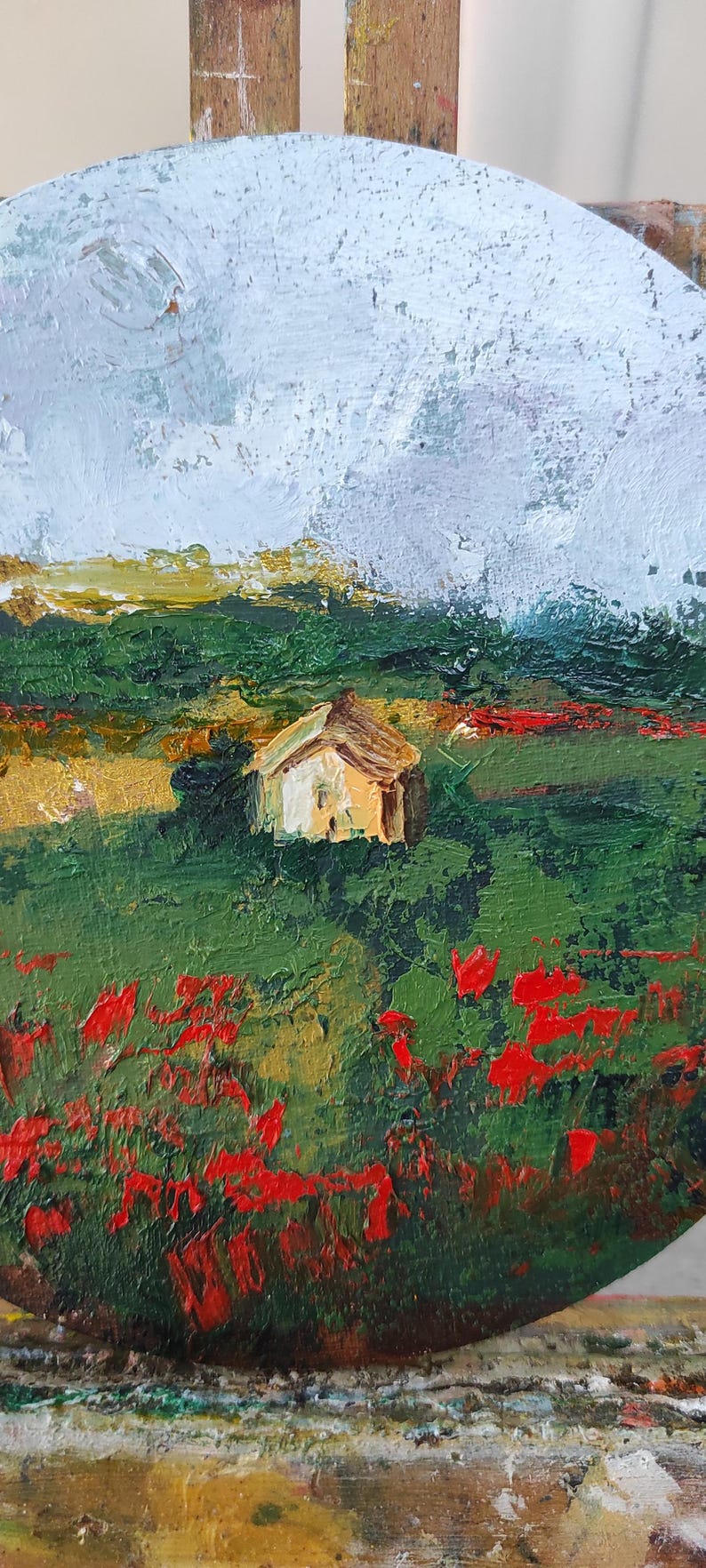 Op de afbeelding: Een schilderij van een klein huis in een veld met rode bloemen en een bewolkte lucht. Het schilderij is gemaakt in een losse, impressionistische stijl.