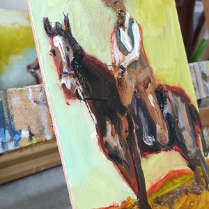 May include: Oil painting of a cowboy on horseback. The artwork features a brown horse and a rider in a hat and vest. The background is a blend of yellow and green, with a hint of red at the bottom. The painting is on a wooden panel.