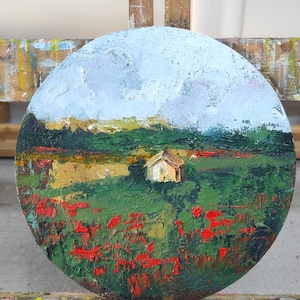 Op de afbeelding: Een rond canvas schilderij van een landschap met een klein huis in de verte. Op de voorgrond is een veld met rode bloemen en groen gras. De lucht is lichtblauw met witte wolken.
