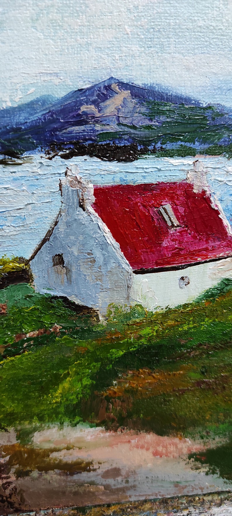 May include: A painting of a white cottage with a red roof, set against a backdrop of a blue mountain range and a body of water. The cottage has a small window and a round opening in the wall. The scene is painted in a loose, impressionistic style.