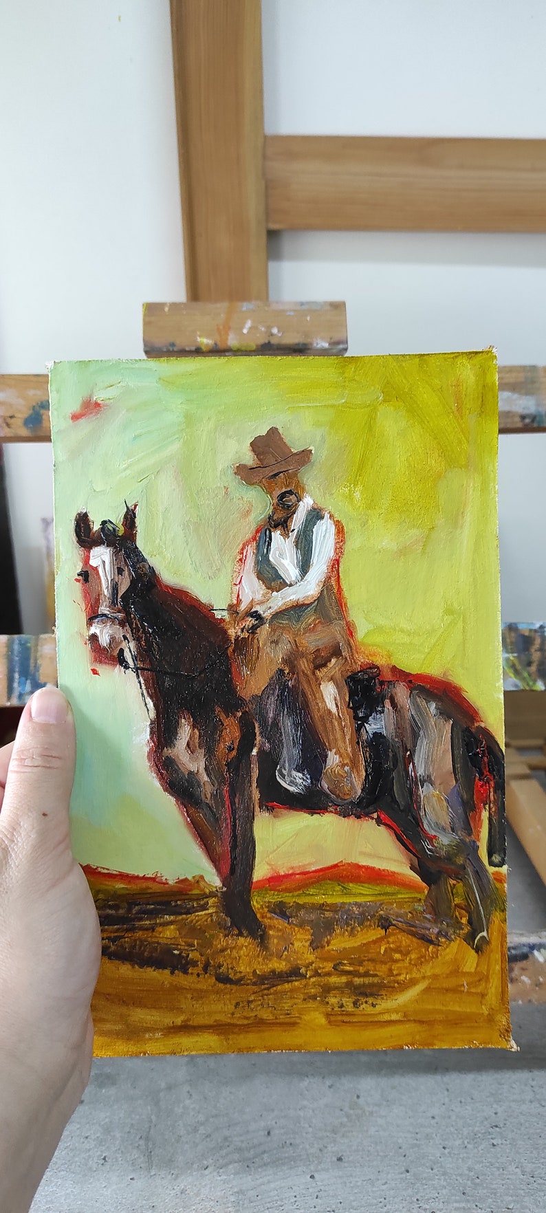 May include: Oil painting of a cowboy riding a horse. The cowboy wears a brown hat, vest, and shirt. The horse is brown and black. The background is yellow and green.