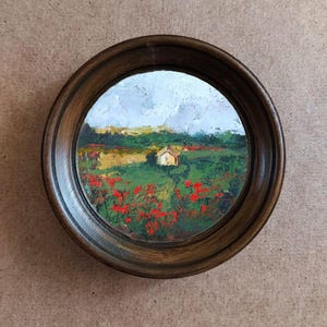 Op de afbeelding: Een ingelijst olieverfschilderij dat een landelijk landschap afbeeldt met een klein huis in de verte, omringd door een veld met rode klaprozen.