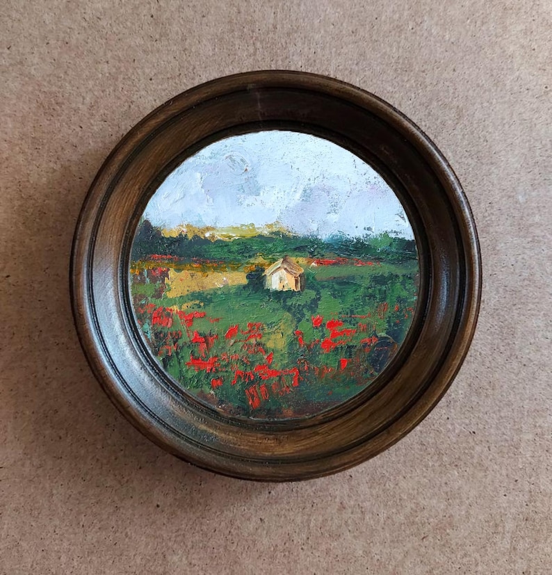 Op de afbeelding: Een ingelijst olieverfschilderij dat een landelijk landschap afbeeldt met een klein huis in de verte, omringd door een veld met rode klaprozen.