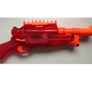 May include: A red and orange Nerf N-Strike Elite Disruptor toy gun with a scope and a magazine. The gun is made of plastic and has a clear red body.