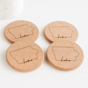 May include: Set of four cork coasters featuring the outline of the state of Iowa with the word "home" inscribed on each coaster.
