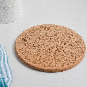 May include: A round cork trivet with a black and white design of coffee cups, coffee beans, and other coffee-related items.