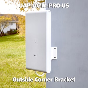 May include: A white UAP-AC-M-PRO-US wireless access point mounted on an outside corner bracket. The bracket is white plastic and is attached to a gray wall.