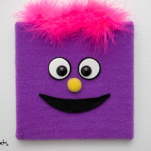 May include: Purple felt puppet with a pink fuzzy hair, white eyes with black pupils, a yellow nose, and a black smiling mouth.