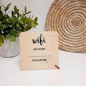 May include: A light-coloured wooden sign with the words "wifi NETWORK PASSWORD" in black. The sign is rectangular with a small wooden dowel. A woven basket and a potted plant are in the background.