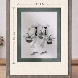 Puede incluir: Obra de arte enmarcada que representa a dos figuras de blanco que llevan cestas de flores. La obra mide 24,5 cm de ancho y 30 cm de alto, enmarcada en un marco gris y crema. Las figuras llevan sombreros cónicos.