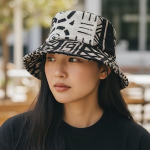 Peut inclure: Un chapeau de pêcheur à motifs noirs et blancs. Le chapeau présente un motif géométrique et un large bord. Le chapeau est fait d'un tissu texturé. La personne porte un haut noir et a de longs cheveux noirs.