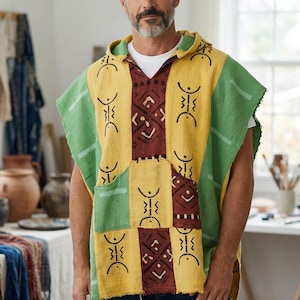 May include: A hooded poncho featuring a patchwork design of yellow, green, and dark red panels. The fabric is decorated with black geometric symbols and line patterns. The garment has a V-neck opening, a front pocket, and frayed edges.
