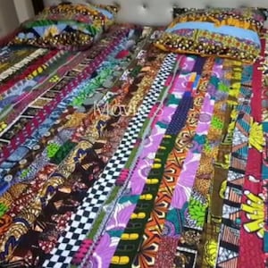 May include: A colourful patchwork quilt featuring a range of patterns and colours, including red, green, yellow and purple. The quilt is made from strips of fabric sewn together to create a distinctive and eye-catching design.