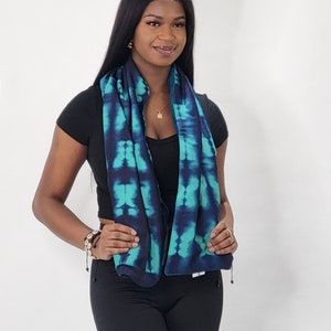 May include: A woman wearing a black top and black pants with a blue and green tie-dye scarf around her neck.