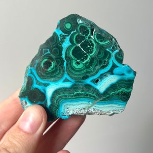 May include: A green and blue malachite stone with a swirling pattern. The stone is smooth and polished.
