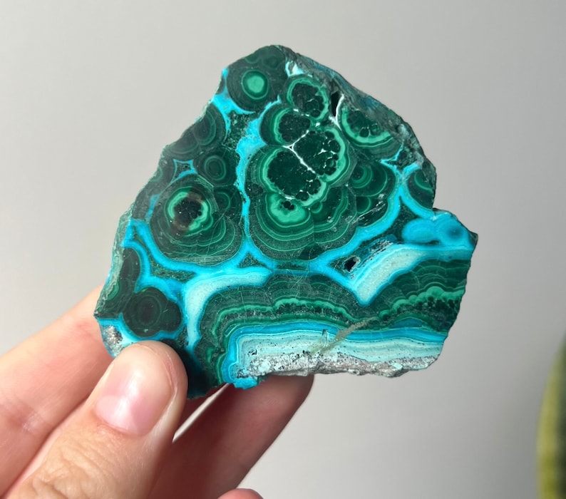 May include: A green and blue malachite stone with a swirling pattern. The stone is smooth and polished.