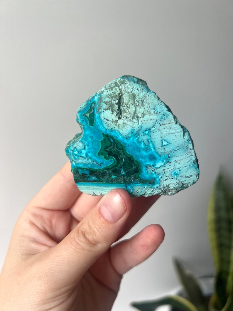 May include: A turquoise and green gemstone with a swirling pattern. The stone is smooth and polished, and it has a natural, organic shape.