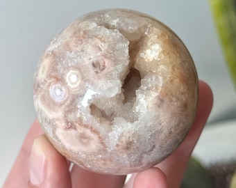 May include: A white and brown agate sphere with a natural crystal geode opening. The geode is lined with white quartz crystals.